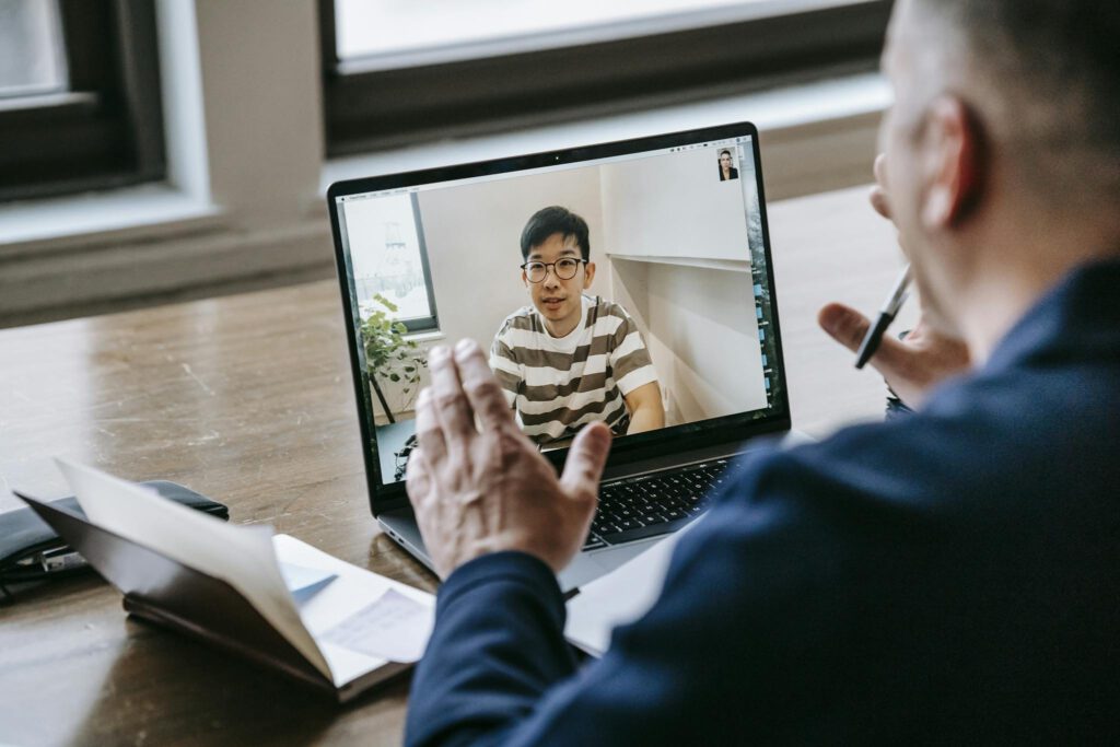 Two professionals engaged in an online video conference on a laptop in an indoor setting.